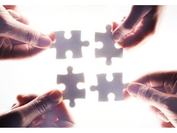 Four hands holding jigsaw pieces.